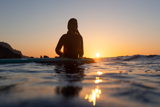 Surfer meisje wacht op een golf in het water bij zonsondergang. Hoge kwaliteit foto - Foto, afbeelding