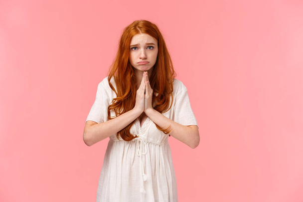 Gloomy and sad, cute pouting redhead girl asking for help, looking hopeful camera, make promise or appologizing, press hands together in pray, begging favour, pleading over pink background. - Photo, Image