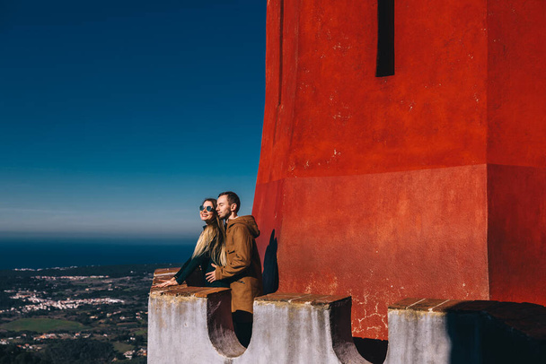 una coppia sognante passeggia intorno al Palazzo Nazionale di Pena, si erge su un balcone e posa sullo sfondo di un muro rosso e di un bellissimo paesaggio., - Foto, immagini