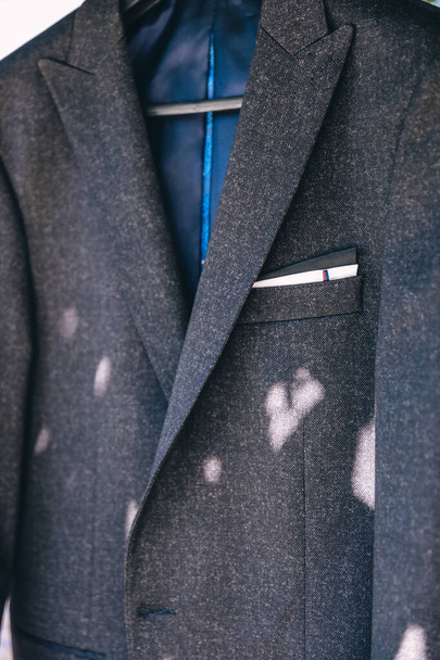 Abrigo de lana gris de lujo para hombres, chaqueta gris, con un gemelo azul, colgado en una percha. - Foto, Imagen