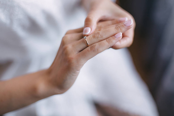 Κοντινό πλάνο ενός χρυσού δαχτυλιδιού με ένα διαμάντι στο χέρι της νύφης με ένα ντελικάτο μανικιούρ. - Φωτογραφία, εικόνα