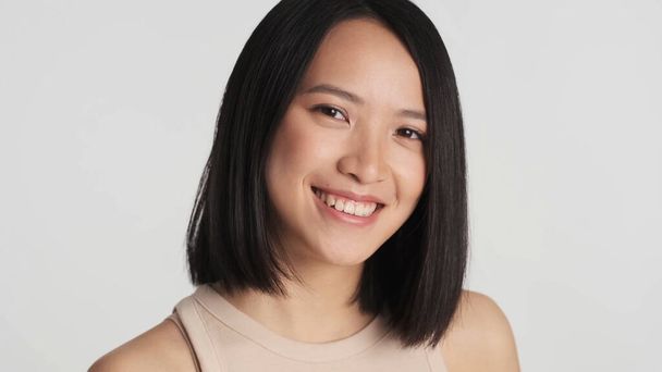 Gros plan belle femme asiatique regardant charmant sourire à la caméra sur fond blanc. Jeune jolie fille asiatique posant en studio - Photo, image