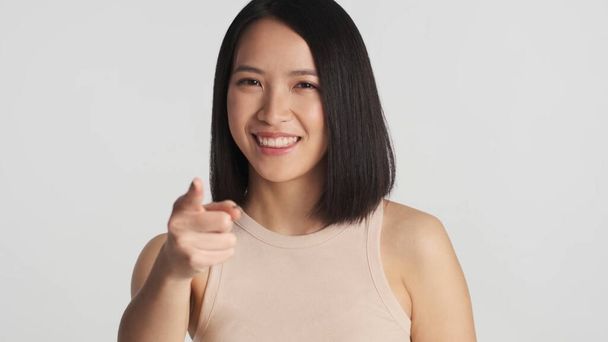 Charmante femme asiatique indiquent directement à la caméra avec index regardant heureux sur fond gris - Photo, image