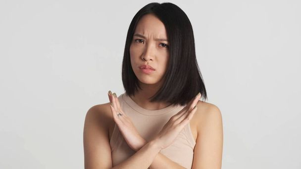 Mujer asiática seria que no muestra ningún gesto en la cámara mirando molesto sobre fondo blanco. Sin expresión - Foto, Imagen