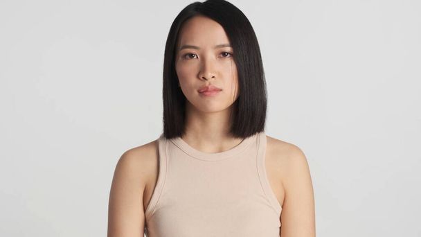 Mladá krásná asijská žena pozorně dívá na kameru stojící nad bílým pozadím. Žena asijské pózování izolované - Fotografie, Obrázek