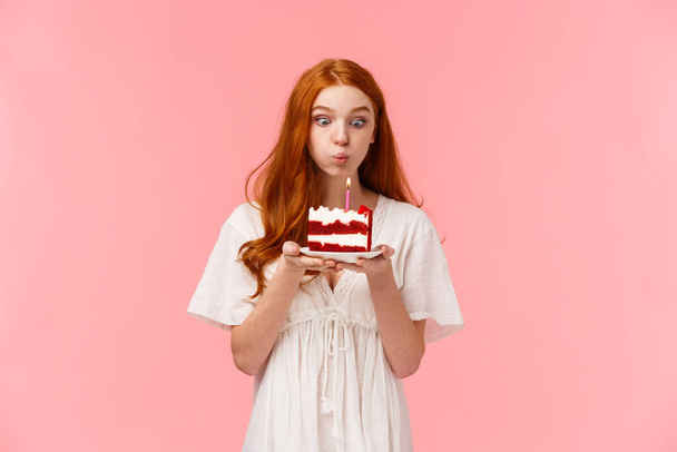 Croyez au miracle. Fille rousse mignonne et stupide souhaitant un anniversaire, soufflant une bougie sur un gâteau de jour-b avec une expression concentrée, s'amusant, faisant la fête et célébrant dans le cercle familial
. - Photo, image