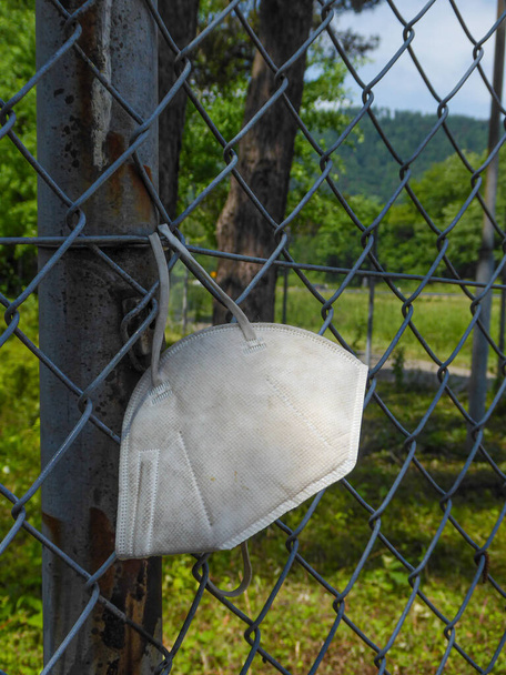 old, dirty and discarded mask hangs on a fence. A symbol of garbage and pollution - Photo, Image