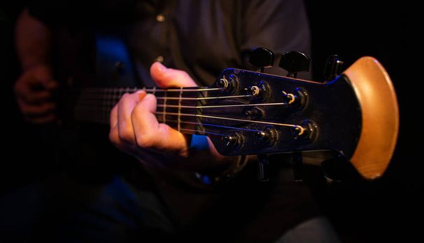 Tiro seletivo de um músico tocando em uma guitarra acústica com as mãos visíveis um foco na cabeça da guitarra - Foto, Imagem