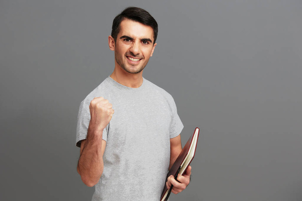 Homem alegre com um livro em suas mãos em um cinza T-shirt emoções fundo cinza. Foto de alta qualidade - Foto, Imagem