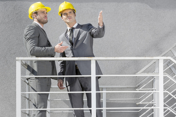 Businessmen in hard hats discussing on stairway - 写真・画像