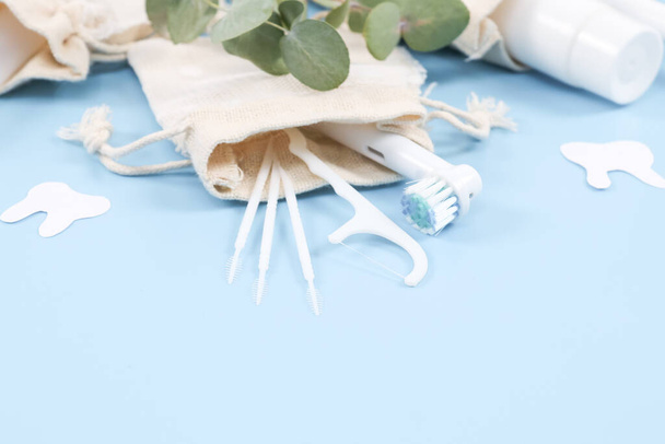 Zestaw szczoteczek do zębów, wykałaczek, nici dentystycznej i pasty do zębów w bawełnianych workach na delikatnym niebieskim tle, widok z bliska. - Zdjęcie, obraz