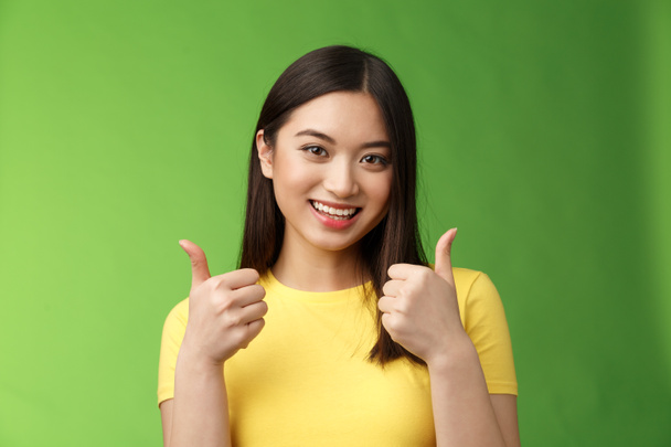 Supportive cute asian girlfriend rooting for lover show thumbs-up approval sign, joyfully smiling, like good choice, accept excellent effort, encourage friend, stand green background. Copy space - Fotografie, Obrázek