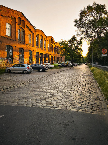 Wroclaw, Polonia - Junio 2021: Hermosa puesta de sol sobre una larga calle llena de coches aparcados junto al antiguo edificio de ladrillo rojo - Foto, Imagen