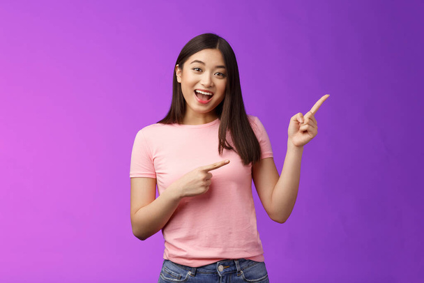 Friendly enthsuasitic amazed attractive tender asian girl having interesting conversation, discuss interest new store, pointing right inviting come inside, stand purple background smiling camera. - Photo, Image