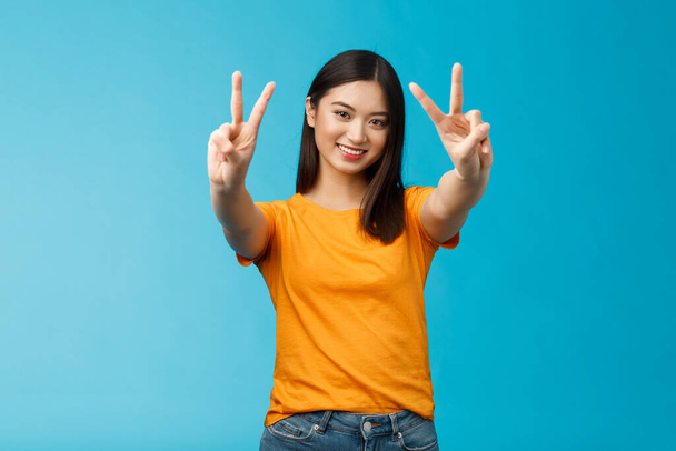Positive upbeat cute asian girl believe win, aim success extend hands show victory, peace sign smiling broadly, have happy enthusiastic mood, spend carefree vacation travel abroad value pacifism. - Photo, Image