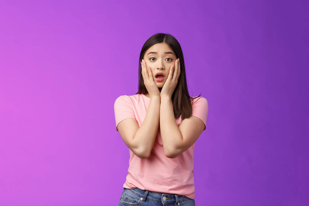Concerned shocked timid insecure asian woman, feel pitty, shame hearing shocking news, grab face sorry for friend, gasping, opened mouth upset, sighing distressed, stand purple background. - Photo, Image