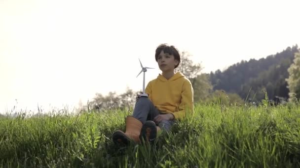 Boy dressed in yellow hoodie keeps model wind turbine in the field. High quality 4k footage - Video