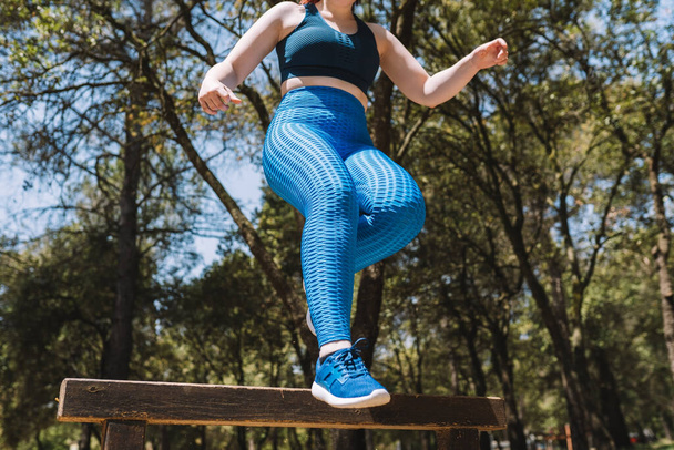 croppet shot van een mooi jong fitnessmeisje, training outdoor horden springen. Een sportieve vrouw die springt. levensstijl gezondheid en welzijn. Natuurlijk zonlicht, achtergrond van natuurlijke vegetatie, bos - Foto, afbeelding