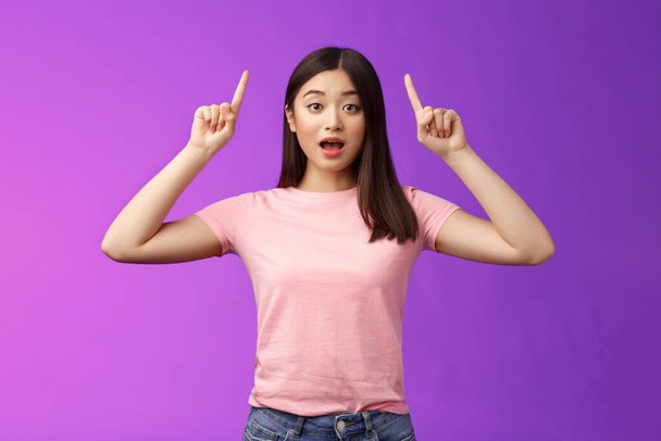 pobudzony słodkie zaskoczony Azji dziewczyna w różowy t-shirt mówi o niesamowite wiadomości wskazując podniesione palce w górę, wskazać top reklamy, otwarte usta zdumiony, podekscytowany stoisko niebieski tło. - Zdjęcie, obraz