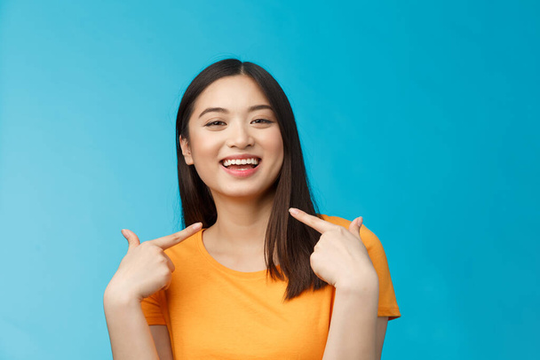 Close-up proud boastful cute asian girl telling story pointing herself, smiling broadly, bragging new haircut, standing pleased, delighted tell big news, stand blue background upbeat. - Photo, Image