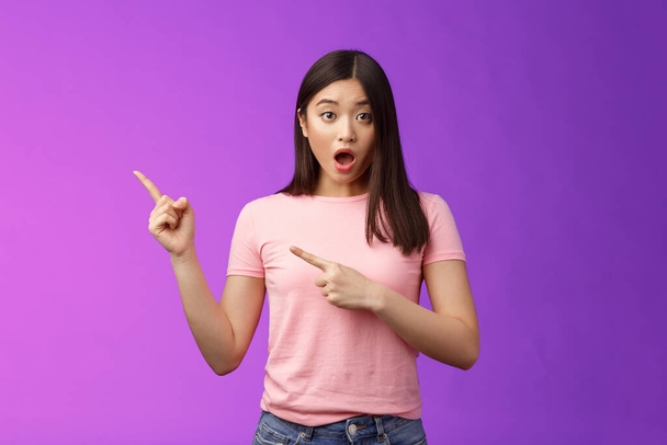 Shocked upset speechless cute asian girl react stunned friend got expensive car, drop jaw astonished, look camera full disbelief, pointing left, discuss astonishing news, stand purple background. - Photo, Image