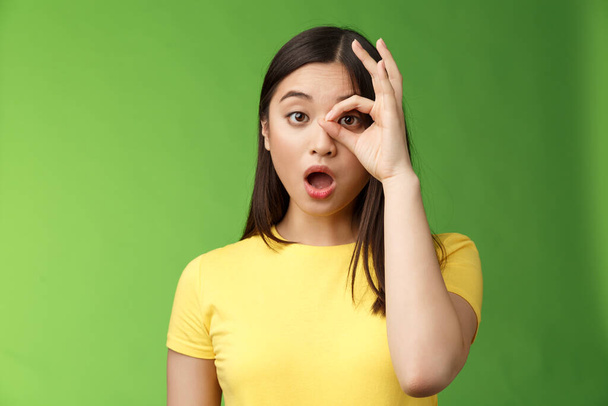 Amazed speechless cute asian young girl drop jaw astonished, look through ok circle sign, drop jaw speechless, impressed look camera, check out incredible promo, stand green background. - Photo, Image