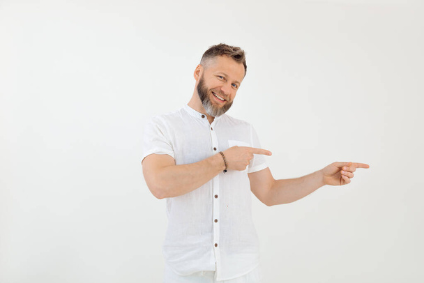 Bearded smiling businessman in white outfit on white isolated background. Showing and presenting new product. Indicate something invisible on empty space by forefingers. Innovative ideas. Copy space - Fotó, kép
