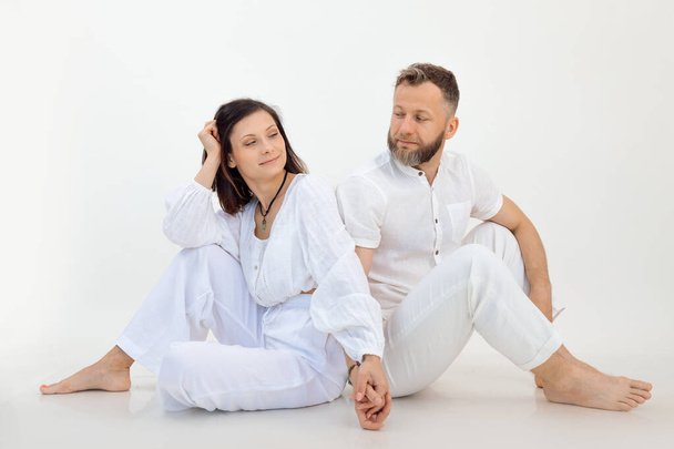 Man and woman on studio shot, couple in white outfit holding hands together. Sit back to back. Spiritual trust. Family relationship therapy. Psychology treatment for married couples, wife and husband - Foto, imagen