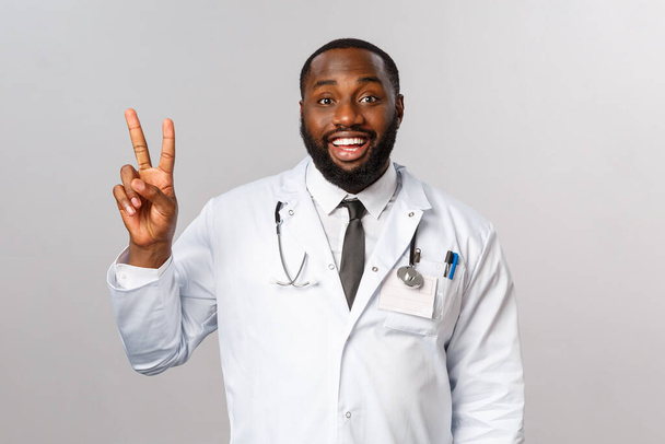 Šťastný, dobře vypadající, nadšený africký americký lékař vysvětluje, jak léčit nemocné pacienty, ukazuje číslo dvě nebo dvě, aby si objednal pro sebe a spolupracovníka v nedaleké kavárně. - Fotografie, Obrázek