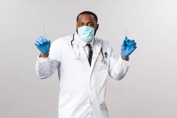 Ковид-19, лечение коронавируса и лабораторная концепция. Забавный молодой афро-американский врач, ученый в латексных перчатках и медицинской маске для лица, держащий пробирки, флакон с вакциной и танцами
. - Фото, изображение