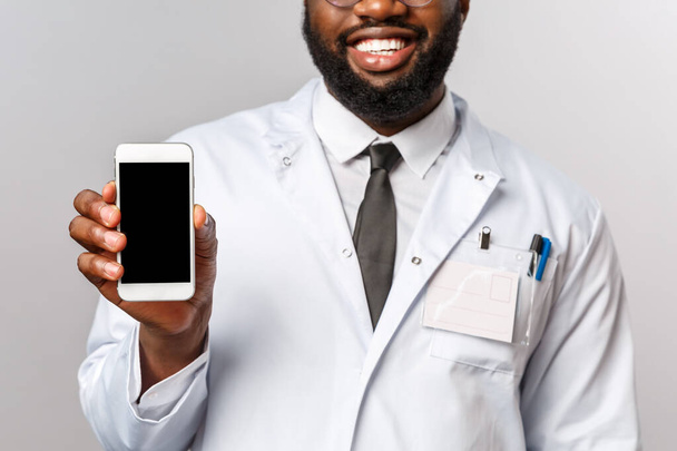 Sağlık, ilaç ve hastane tedavi konsepti. Gülümseyen bir doktor, Afrikalı Amerikalı terapist cep telefonu uygulaması kullanarak doktorla görüşmeyi öneriyor.. - Fotoğraf, Görsel