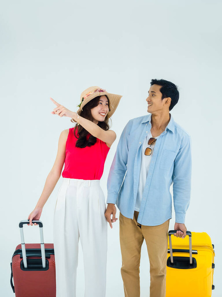 Exciting travel, happy holiday. Summer vacation. Asian couple travelers looking each other with exciting, Man and young woman pointing with suitcases on trip, isolated on white background, vertical. - Photo, Image