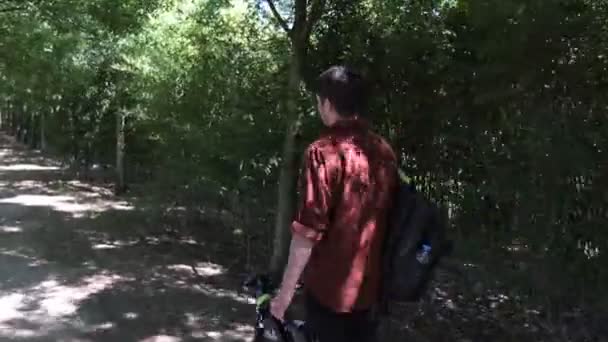 Giovane uomo che trasporta attrezzature video, cameraman riprese in foresta portando forniture, cineasti che lavorano nel verde - Filmati, video