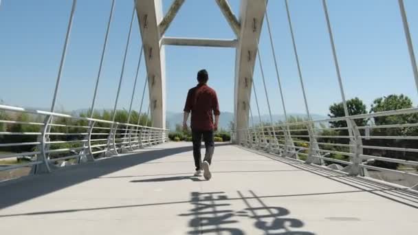 Köprüyü geçen genç adam, köprüyü geçen genç adam, metal köprüden geçen kırmızı gömlekli adam. - Video, Çekim