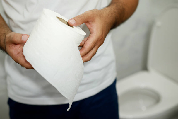 El hombre sufre de diarrea mano mantenga papel de seda rollo delante del inodoro. estreñimiento en el baño. Tratamiento dolor de estómago e higiene, atención médica  - Foto, Imagen