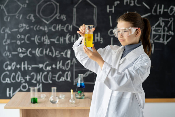 дівчинка-студент вивчає дослідження і проводить хімічний експеримент, роблячи аналіз і змішування рідини в склі в класі. Освіта і наука концепція
 - Фото, зображення