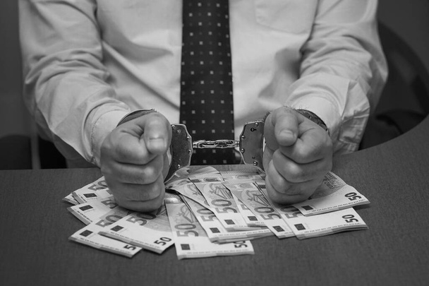 Mani di impiegati in manette in possesso di una mazzetta di banconote in euro. Primo piano in bianco e nero fotografia uomo mani in manette - Foto, immagini