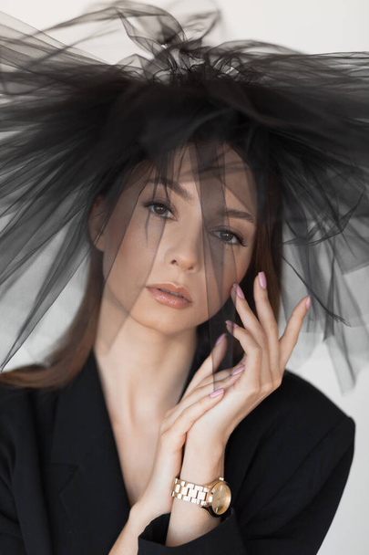 Vertical portrait of attractive, mystery, sad and serious brunette woman, posing and looking at camera in black dress and veil hat. Widow on funerals. Mourning outfit. Sadness from loss. Close up - Photo, Image