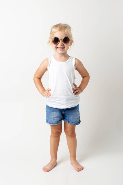 Blond child in sunglasses posing on a light background in the studio. - Zdjęcie, obraz