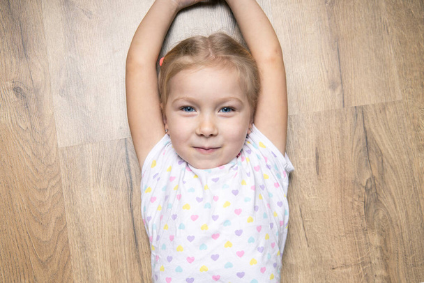 Gyönyörű kislány felemelte a kezét egy fapadlón fekve. Felülnézet, lapos fektetés - Fotó, kép