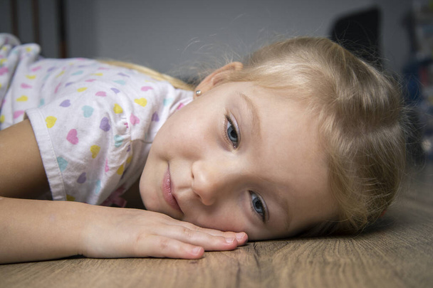 Грустная красивая девочка в футболке, лежащей на деревянном полу - Фото, изображение