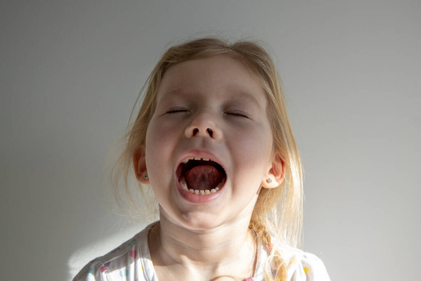 Krzycząca dziewczynka z zamkniętymi oczami na tle białej ściany - Zdjęcie, obraz