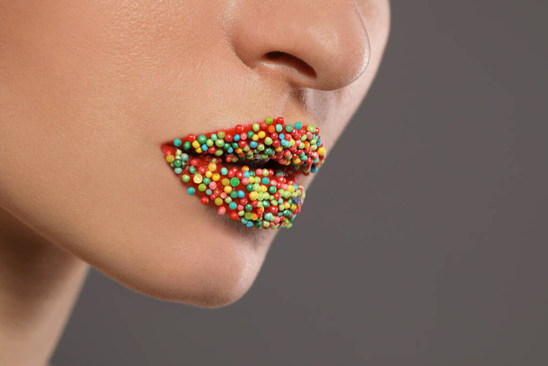 Young woman with beautiful lips covered confectionery sprinkles on gray background, closeup - Fotoğraf, Görsel