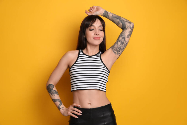 Beautiful woman with tattoos on arms against yellow background - Zdjęcie, obraz