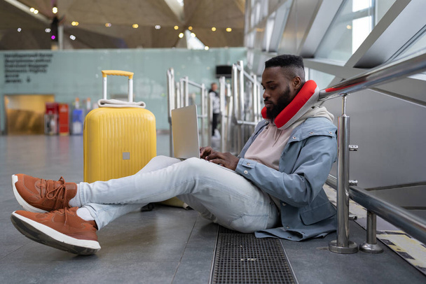 Freelancer masculino afro-americano sério concentrando-se em rede, projeto trabalhando no laptop, se comunicando nas mídias sociais, procurando informações on-line enquanto está sentado no aeroporto ou na estação ferroviária.  - Foto, Imagem