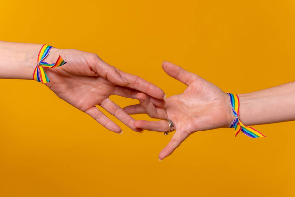 Detail of two hands of two women caressing and touching each other's fingers, LGBT concept on a yellow background, couple of lesbian girls - Foto, Bild