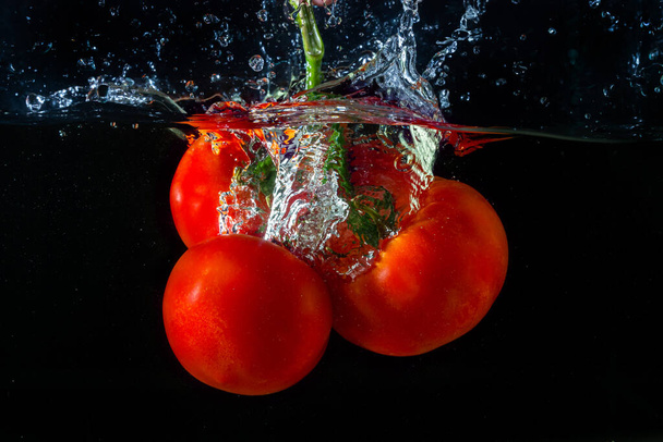 Свіжий червоний помідор падає у воду з бризками води і повітряними бульбашками ізольовані на чорному тлі
. - Фото, зображення