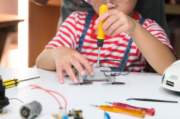 Skoncentrowana dziewczynka naprawia swojego drona zabawki z narzędziem w ręku i starannie montuje drona zabawki ze śrubokrętem. Zainteresowania STEM dla zaawansowanych inteligentnych dzieci. - Zdjęcie, obraz
