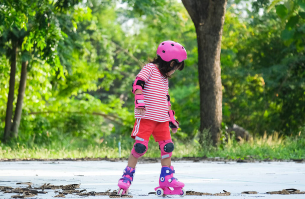 Roztomilá asijská holčička v ochranných podložkách a bezpečnostní přilbě cvičit kolečkové brusle v parku. Vzrušující outdoorové aktivity pro děti. - Fotografie, Obrázek
