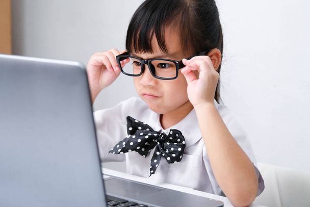 Cute Asian little girl gra nauczyciel gry role lub małej bizneswoman pracy z laptopem w biurze. Nauka i zabawa dla dzieci w domu. - Zdjęcie, obraz